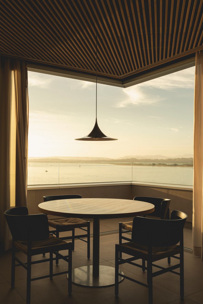 Dining tables overlooking views of the bay from a frameless corner window inside a brutalist restaurant in Spain by Zooco Estudio