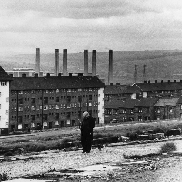 Photo of person walking in front of buildings and chimneys