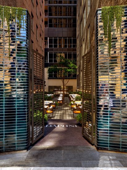 Columns of blue-purple iridescent tiles form a gateway into an alley-like outdoor terrace