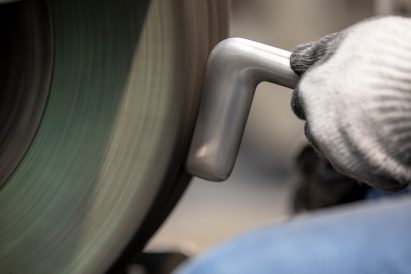 Close-up photo of a worker polishing a silver-coloured metal door handle