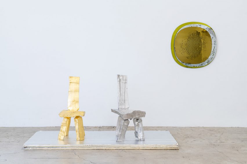 A gold and silver chair with shiny wall hanging