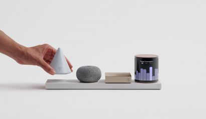 Photo of a hand grabbing a small, inverted cone-shaped light grey object from a rectangular base plate containing three other small objects