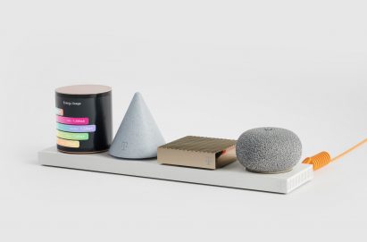 Photo of Layer's Concept Level prototype showing a cylindrical module wrapped in a screen displaying a colourful bar graph, an inverted cone-shaped light grey module, a slim gold bar module and a squashed ball-shaped module with a textured silver surface, all sat on a white base plate. The base is attached to a bright orange wire