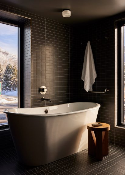 Bathroom with dark green tiles and freestanding white bathtub