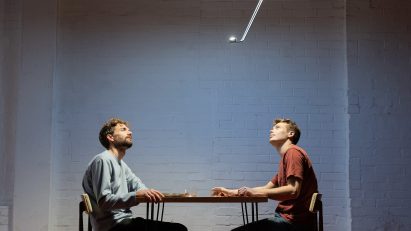 Photo of the Sunday Light creators Nat Martin and Sean Hammett sitting under their product, a bright disc suspended on the ceiling