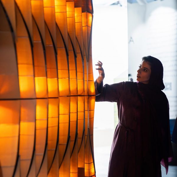 A photograph of a person interacting with an orange light installation.