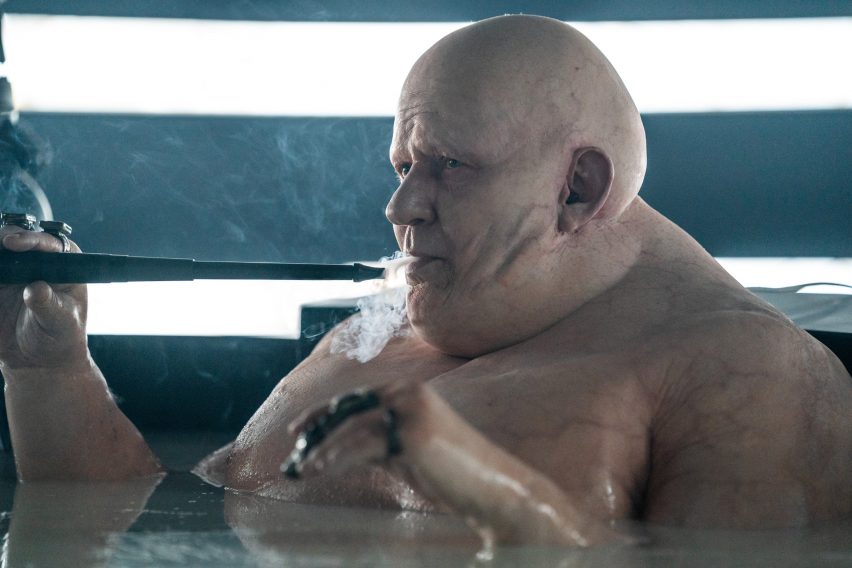 Dune Part Two production photo of Baron Vladimir Harkonnen bathing in sludgy black oil in a dark room striped with fluorescent light