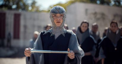 Dune Part Two production photo showing Princess Irulan looking shocked while holding a scroll in a leafy outdoor setting
