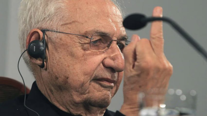 Frank Gehry holding up his middle finger at a press conference