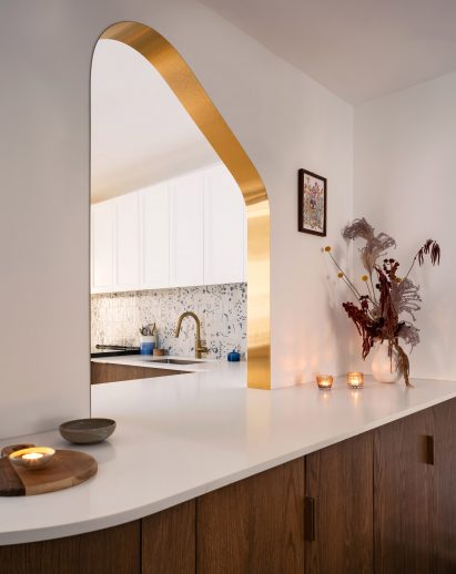 Brass-edged asymmetric portal looking into a kitchen