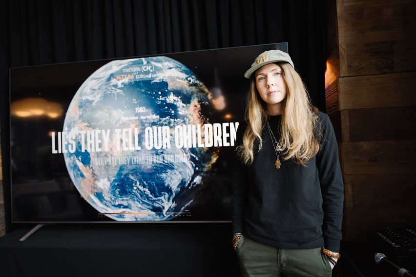 Photo of Beatie Wolf standing next to a screen displaying her Smoke and Mirrors installation
