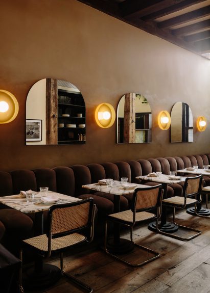 Row of custom mirrors alternated with disk-shaped sconces above tables