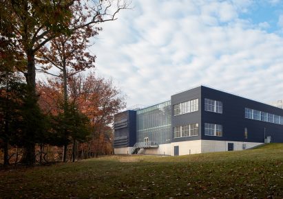 Black building with glass middle and concrete base with fall foilage