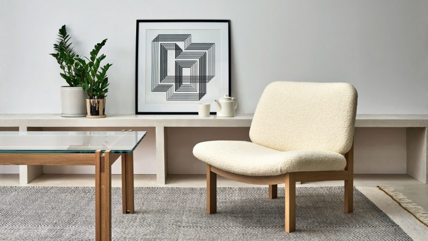 Photo of an armchair and a side table with a carpet under them and a plant and painting in the background