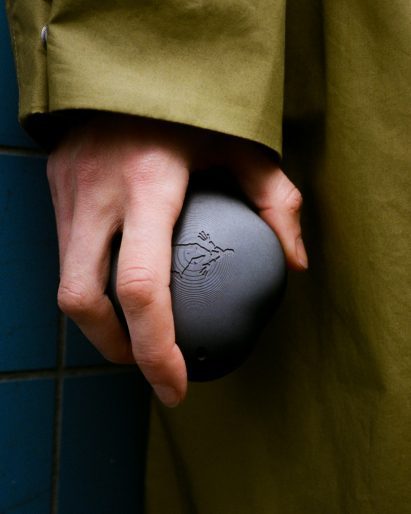 Photo of a hand clutching a dark grey rock-like device emblazoned with the figure of a person walking