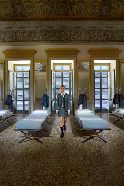 A model wearing a Thom Browne suits walks between the beds