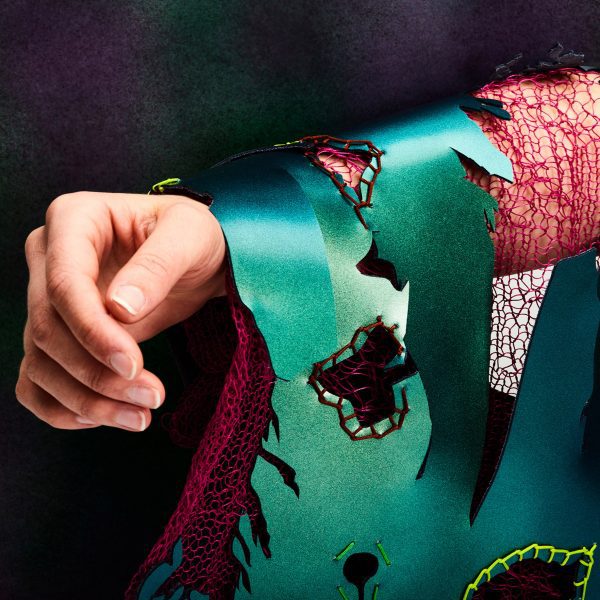 A person's arm wearing torn fabric in green and red tones.