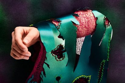 A person's arm wearing torn fabric in green and red tones.