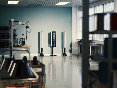 Photo of a restored and recoloured Beosound 9000 six-CD player stand-mounted vertically with a long speaker on either side, on display within a factory