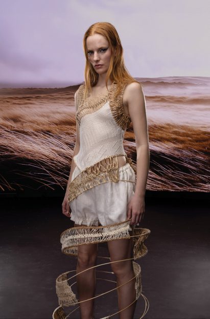 Model wearing white garment in front of landscape-printed backdrop
