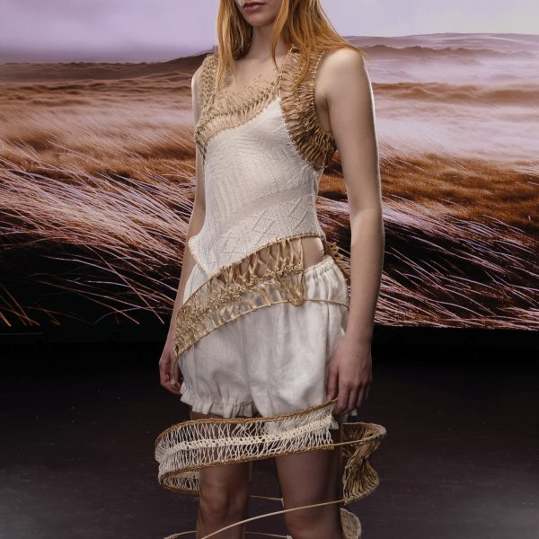 Model wearing white garment in front of landscape-printed backdrop