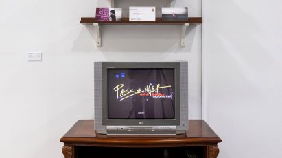 A photograph of a dark brown cabinet against a white wall with a television on top, with three dark brown shelves above.