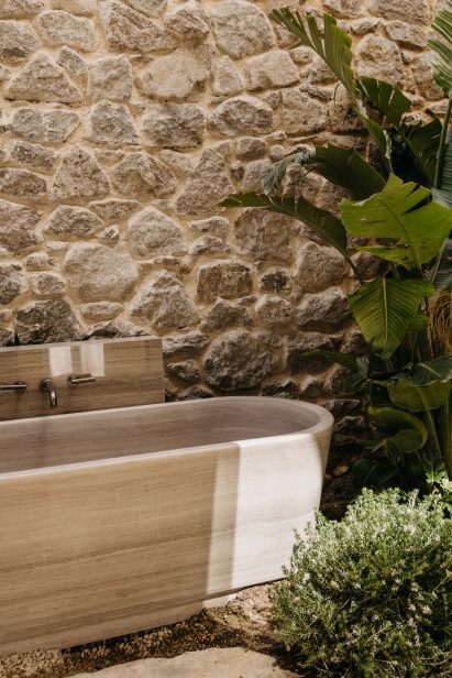 Outdoor bathtub against a stone wall and plants