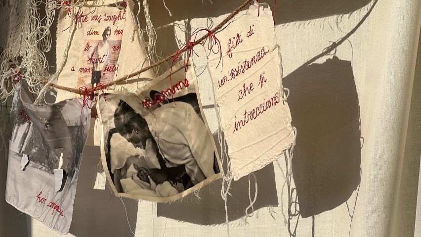 A photograph of various textile sheets hanging from threads. They feature images and red embroidery on them.
