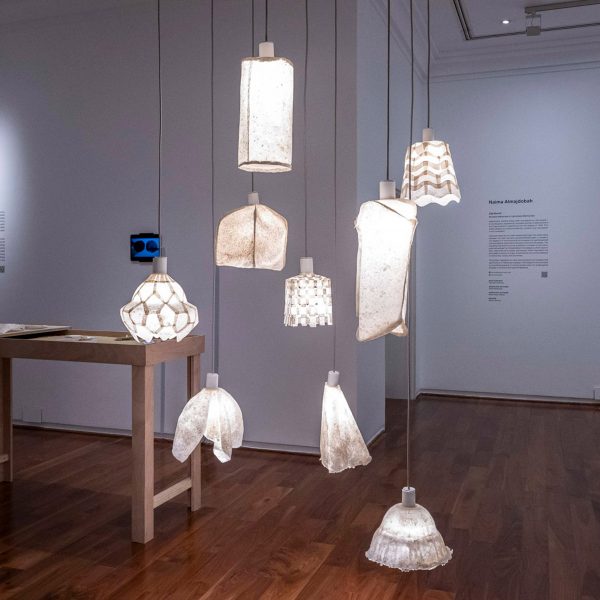 Several white lamps hanging from a ceiling, reflecting onto a brown wooden floor in a room with white walls.