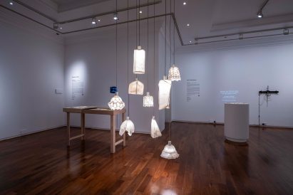 Several white lamps hanging from a ceiling, reflecting onto a brown wooden floor in a room with white walls.