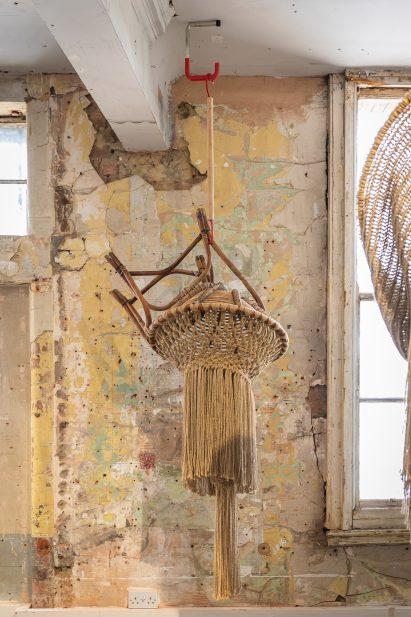 Photo of Christopher Kelly's Interwoven: Dis/Functional No.2 sculpture hanging from a ceiling and showing a chair frame merging with a corcheted and tasselled jute form