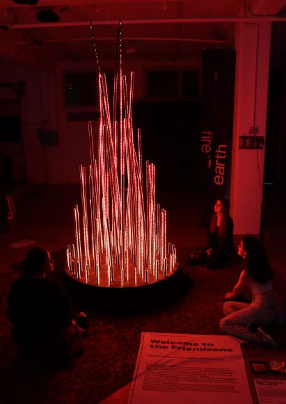 A photograph in tones of red showing people sitting around a circular light installation.