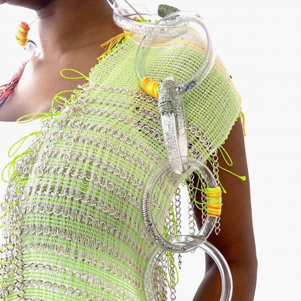A photograph of a person, standing against a white background, wearing a green and silver garment with a large transparent plastic chain draped over their shoulder.