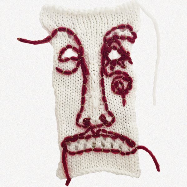 White knitted piece of fabric with red face sewn into it