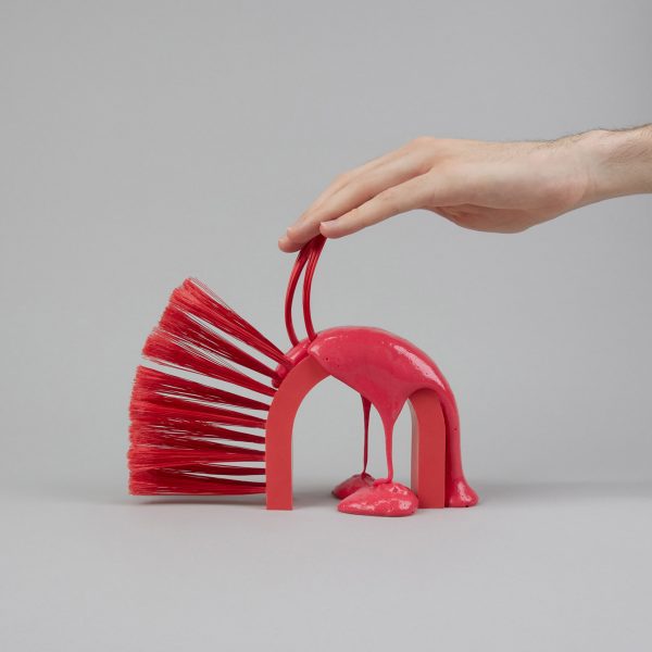 A photograph of a person's hand interacting with a handle attached to a red object, against a grey background.