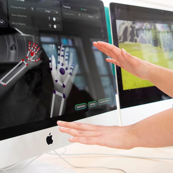 A photograph of a person's hands in front of a computer screen, which is displaying a digital image of hands in colours of red and purple.