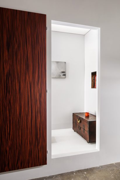 White exhibition space with a wooden trunk and an open wood door
