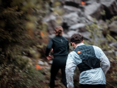 A blurred photograph from behind of two people running through greenery, with a digital diagram of a target on one of the people's backs.
