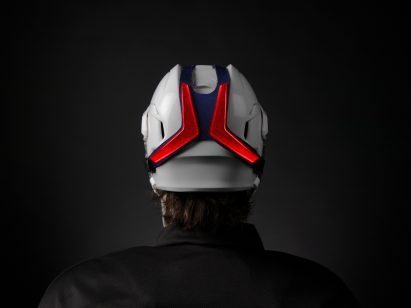A photograph showing the back of a person's shoulders and head, in tones of black, wearing a white and red helmet.