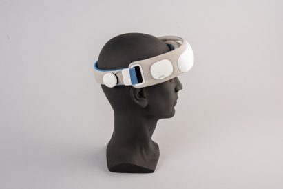 A photograph of a black mannequin head with a device in tones of grey, white and blue wrapped around it.