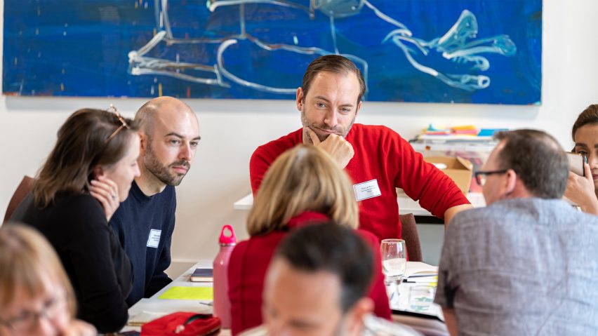 A photograph of people interacting, sat at a desk.