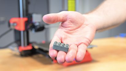 Photo of a hand holding a Lego-like small brick that is grey and has a rougher surface texture than usual