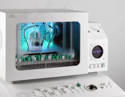 Photo of the Future Fan Stage by Love Hulten showing a tiny stage within a white console, with a small vessel of ferrofluid forming a pattern in the centre of the stage and rows of test tubes in front of the stage