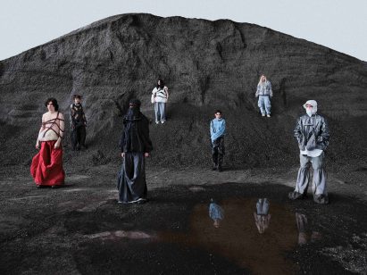A photograph of seven people modelling a student fashion collection against a backdrop of a black cliff and black sand.