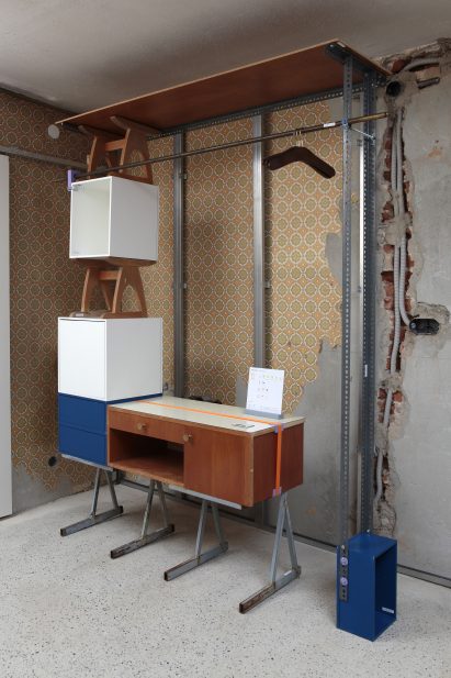 A photograph of a structure consisting of various pieces of furniture, including tables and shelves, in tones of brown, white and blue.