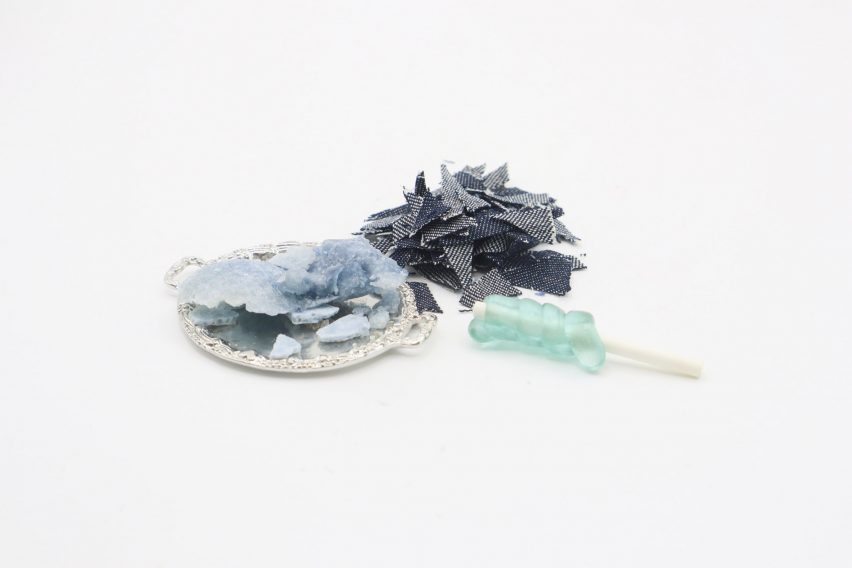 Photo of small scraps of denim fabric, next to a small platter of fabric in the process of being broken down by enzymes, next to a small lollipop-like sweet with light-blue hardened sugar spiralled around a rod