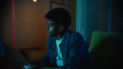 Photo of a young man wearing the Friend necklace around his neck while gaming in a darkened room