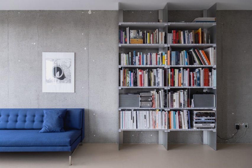 Bookcase and blue sofa in living area with concrete walls