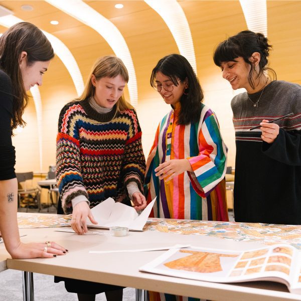 Photograph of four students gathered around a table looking at work.