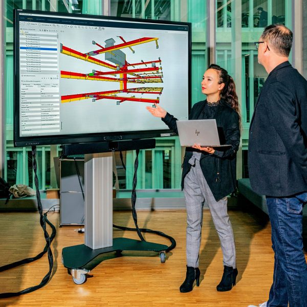 Photograph of a student presenting her work to two others on a large screen.